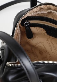 Zwarte leren tas met ritsluiting. Het interieur heeft een beige voering met een bedrukt logo, een ritsvak en een klein leren label voor organisatie.