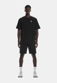 Tricou negru cu mânecă scurtă și un mic logo alb pe piept, asortat cu pantaloni șort negri. Hainele sunt confecționate dintr-un material ușor.