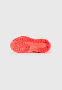 Semelle rouge vif d'une chaussure de sport montrant des motifs de relief ondulés et un petit texte en relief "AMÉLIORER VOTRE MEILLEUR" sur un fond blanc propre.