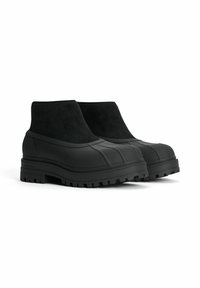 Svarta ankelboots med gummisålar, med en slät yta och en overdel i mocka. Tjockt mönster ger bra grepp; minimalistisk design.