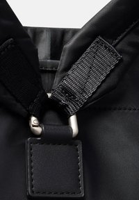 Primo piano di una cintura in nylon nera con una patch in pelle cucita attaccata a una fibbia in metallo argento su un tessuto nero.