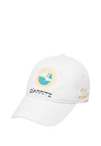White baseball cap featuring a circular embroidered design with a sun, ocean, and lighthouse, and "BIARRITZ" and "ATLAS x ROXY" text.