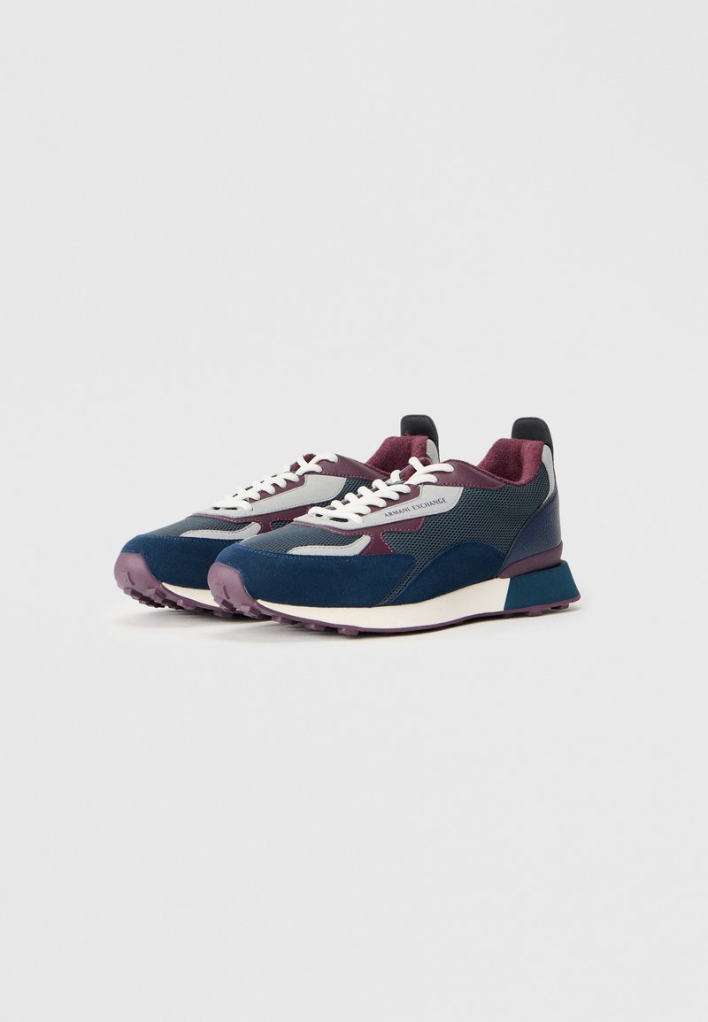 Une paire de baskets basses en marine, gris et bordeaux avec des lacets blancs et un logo "Armani Exchange" sur le côté.