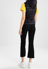 Czarna kamizelka puchowa z kapturem na żółtej koszulce; zestawiona z czarnymi ściągaczami w kratę i białymi trampkami. Prosty i funkcjonalny design.