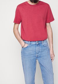 T-shirt di cotone rosso con scollo rotondo, maniche corte, abbinata a jeans in denim blu chiaro con tasca frontale e leggere abrasioni.