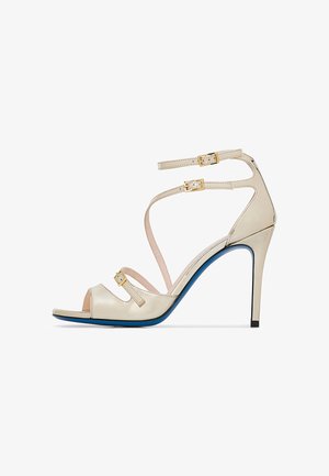 Beige Riemchen-Pumps mit offenem Zehenbereich, goldenen Hardware-Akzenten, blauer Sohle und einem eleganten Design mit mehreren verstellbaren Riemen.