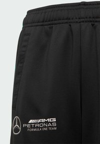 Mustat urheiluleggingsit, joissa on joustava vyötärö ja valkoisella tekstillä ja emblemillä varustettu logo AMG Petronas Formula One Teamille.