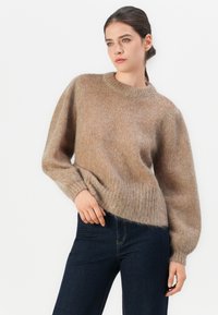 Maglione lavorato a maglia marrone chiaro con scollatura tonda, maniche a palloncino e orlo a coste. Indossato sopra jeans scuri. Texture morbida e pelosa visibile.