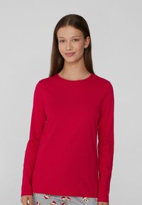 Chemise à manches longues d'un rouge vif, fabriquée en coton doux. Munie d'un col rond et d'une coupe décontractée. Associée à un pantalon de pyjama gris.