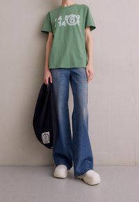 Groene katoenen T-shirt met witte gedrukte cijfers, gecombineerd met flared blauwe jeans en witte plateauschoenen. Zwarte tas met logodetail.