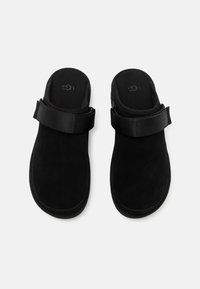 Black suede slip-on sandals with a thick adjustable strap. Soft texture, rounded shape, and molded footbed for comfort. Simple and modern design.