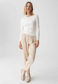 Weißes Langarmoberteil mit rundem Ausschnitt, kombiniert mit hellbeigen strukturierten weitem Hosen und beigen Sneakers mit braunen Akzenten.