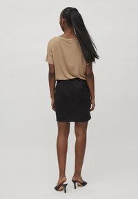 Beige, kortärmad topp matchad med en svart, figurnära kjol. Modellen bär svarta sandaletter med öppen tå. Långt, rakt hår når till midjan.