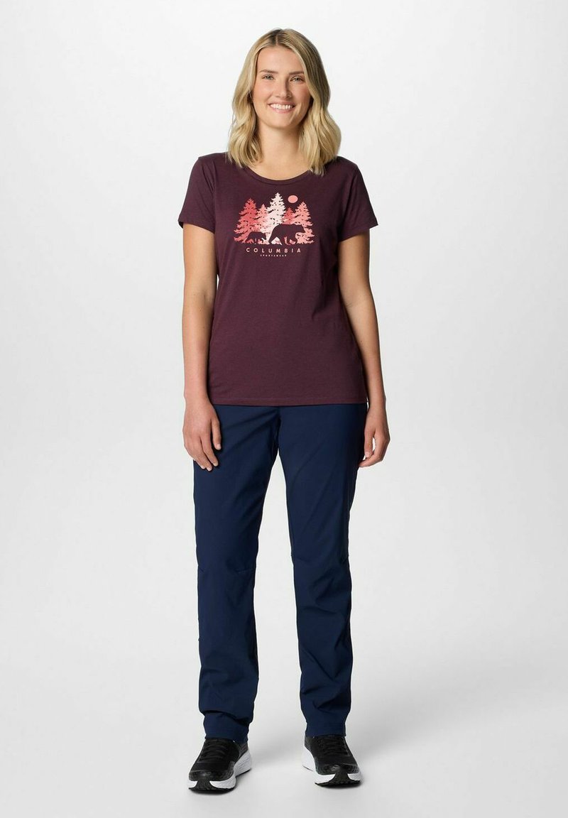 Bordowa koszulka z krótkim rękawem z grafiką przedstawiającą drzewa i niedźwiedzia. W połączeniu z granatowymi, lekkimi spodniami outdoorowymi. Czarne buty sportowe.