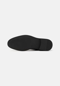 Suela de zapato negra con patrón de agarre texturizado, bordes suaves y punta redondeada. Talón reforzado y diseño minimalista característico.