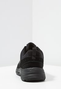 Baskets de sport noires avec une tige en mesh texturé et en suède, semelle rembourrée et une languette au talon ; présente un design élégant et épuré.