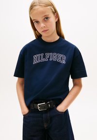 Μπλε βαμβακερό μπλουζάκι με κοντά μανίκια και στρογγυλή λαιμόκοψη, με την επιγραφή "HILFIGER" τυπωμένη με λευκά έντονα γράμματα στο στήθος.