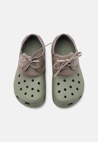 Ζευγάρι πράσινων και καφέ αεριζόμενων λαστιχένιων παπουτσιών με κορδόνια, σχεδιασμένα για καθημερινή χρήση, απεικονισμένα από πάνω σε λευκό φόντο.