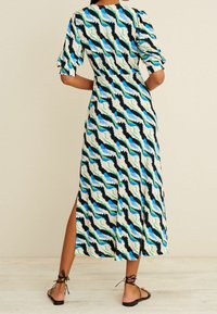 Maxi sukienka w falisty wzór w odcieniach niebieskiego, zielonego i czarnego na kremowym tle; posiada krótkie bufiaste rękawy i boczne rozcięcie.