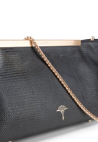 Borsa a tracolla nera con trama, dotata di una cornice metallica dorata e una catena. Presenta un emblema floreale dorato alla base.
