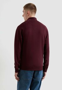Felpa bordeaux con colletto, maniche raglan e polsini a coste, realizzata in tessuto morbido. Abbinata a jeans in denim blu.