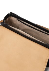 Brun läderhandväska med svart kant, med en slät yta och ett flerkammarinredning, fodrad med beige mönstrad tyg.