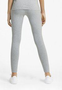 Grå bomullstights med en slät yta och en åtsittande design, parat med vita sportskor. Bakifrån syns att de går till anklarna.