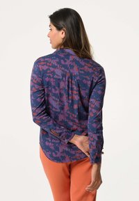 Langsleeve shirt in navy met roze en paarse abstracte patronen, met knoopmanchetten, kraag en een plooi aan de achterkant. Gecombineerd met oranje broek.