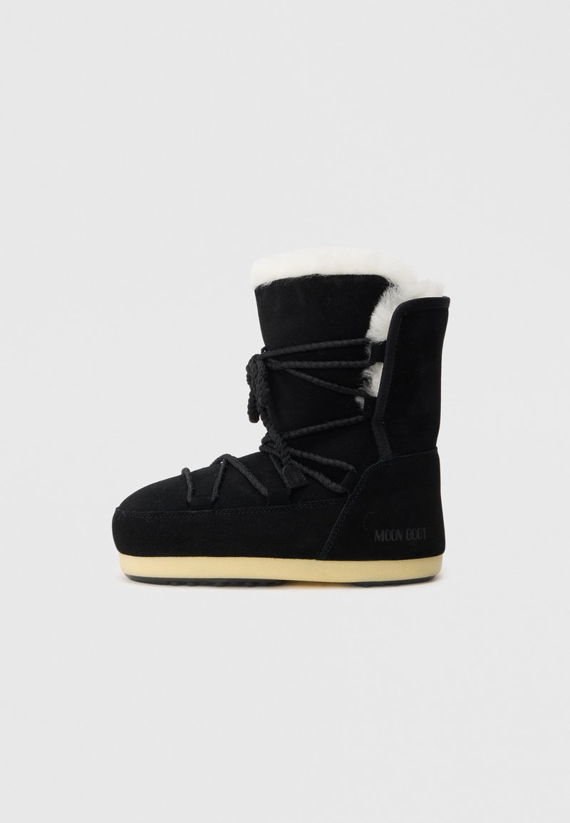 Botte en suede noire avec une doublure en fourrure blanche, présentant un laçage à l'avant, un support de cheville rembourré et une semelle en caoutchouc pour l'adhérence.