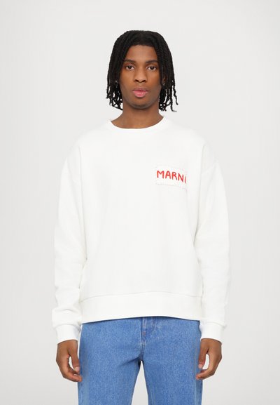 Weißes Sweatshirt mit rundem Ausschnitt und einer Fronttasche, die roten "MARNI"-Text trägt. Aus Baumwollmaterial und lockerer Passform. Kombiniert mit blauen Jeans.
