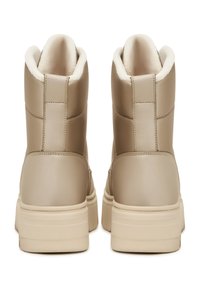 Zapatillas altas de imitación de cuero beige con una textura suave, cuello acolchado y una suela gruesa de un beige claro. Acolchado interior suave visible.