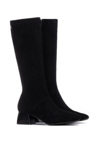 Botas de ante negras hasta la rodilla con punta afilada y un tacón bajo. Cuenta con una cremallera lateral para facilitar su uso. Textura suave y mate.