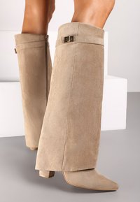 Bottines en suède beige à bout pointu et talon bloc, présentant un design replié et des accents en métal doré.