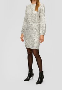 Silver, paljetterklänning med långa, puffiga ärmar och figurnära midja. Bärs med svarta, klackade ankelskor och genomskinliga svarta strumpbyxor.