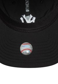 Schwarze Baseballkappe mit flacher Krempe, strukturiertem Stoff, Innenetikett und einem Authentifizierungsaufkleber mit einem Baseball-Design.