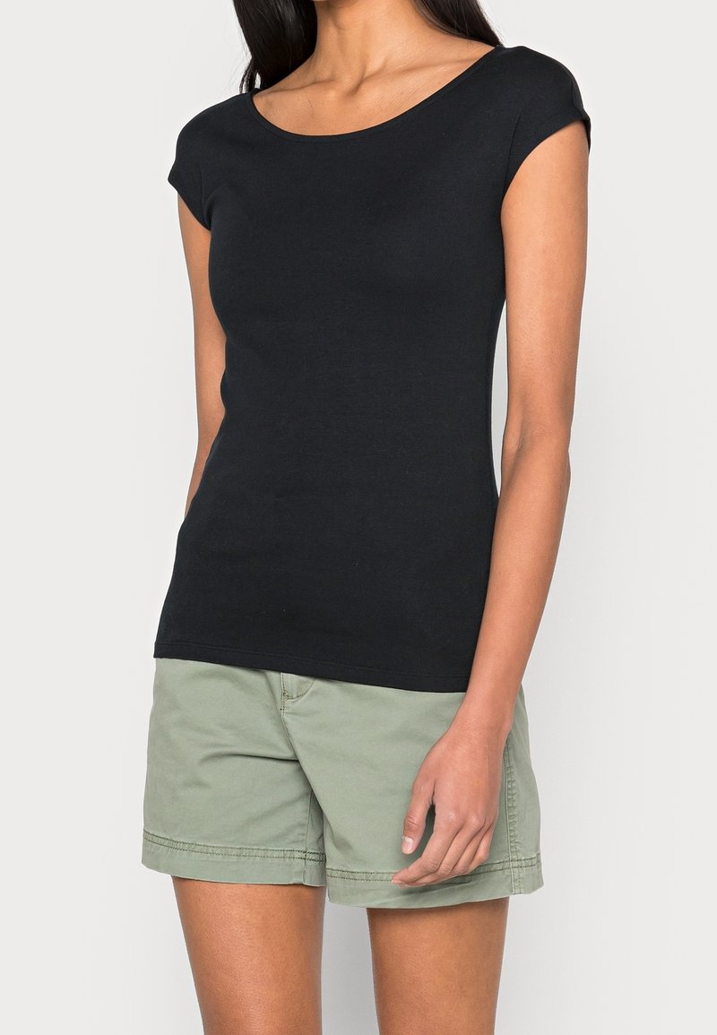 T-shirt noir moulant avec un col dégagé et des manches courtes, associé à un short en coton vert clair. Tissu doux, design minimaliste.
