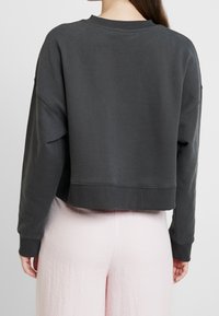 Cropped sweatshirt in dark gray cotton blend, featuring dropped shoulders, a wide neck, and ribbed cuffs. Paired with light pink pants.