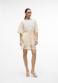 Abito in pizzo color beige chiaro con scollatura a V, maniche corte e vita regolabile; motivo a zigzag intricato e tessuto trasparente in tutto l'abito.