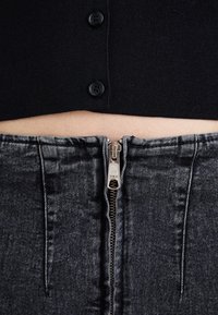 Svart stickad topp med tre knappar ovanför en grå denimkjol med en silver YKK-dragkedja i mitten och sydda detaljer på sidorna.