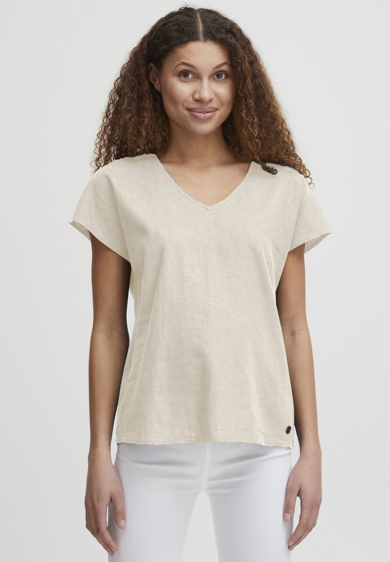 Beige lin T-skjorte med V-hals, korte ermer og avslappet passform. Har synlige sømmer og en liten logo på kanten.