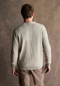 Light gray knitted sweater with a textured finish, featuring a round neckline and ribbed cuffs, worn over beige trousers.