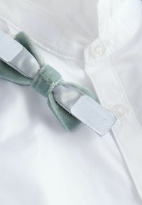 Svilena pentlja iz svetlo modrega žameta in satena z belim ježkom na ovratniku bele srajce z gumbi.