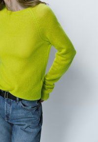 Pull tricoté jaune-vert vif avec un col rond et des manches longues, associé à un jean en denim bleu clair.