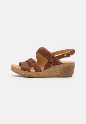 Brun kile-sandal med flettede læderremme, justerbar ankelspænde og sål med korktekstur.