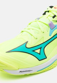 Zapatilla de running verde lima con parte superior de malla, acentos turquesa, líneas delgadas negras y suela blanca con el texto "Mizuno Enerzy".