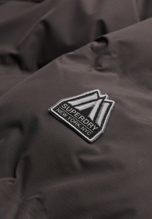 Dark gray fabric with a subtle texture features an embroidered patch with a triangular design, reading "SUPERDRY" and "NEW YORK.NYC."