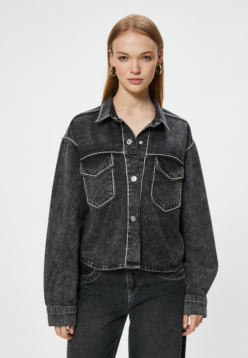 Svart denimjacka med en kortad design, kontrasterande vita sömmar, två bröstfickor och knäppning; har en krage och en avslappnad passform.