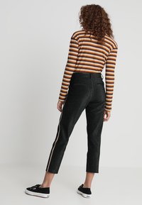 Pantalon court noir pailleté avec une bande latérale dorée, associé à un haut à manches longues marron et blanc rayé. Des baskets noires complètent le look.