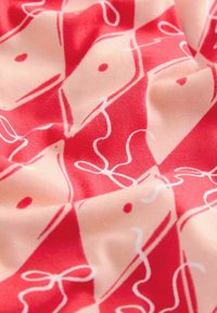 Cotton fabric with a red and pink geometric pattern featuring white abstract shapes, swirls, and dots, creating a textured visual effect.