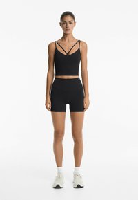 Black two-piece activewear set featuring a cropped tank top with crisscross straps and high-waisted shorts. Smooth, stretchy fabric.